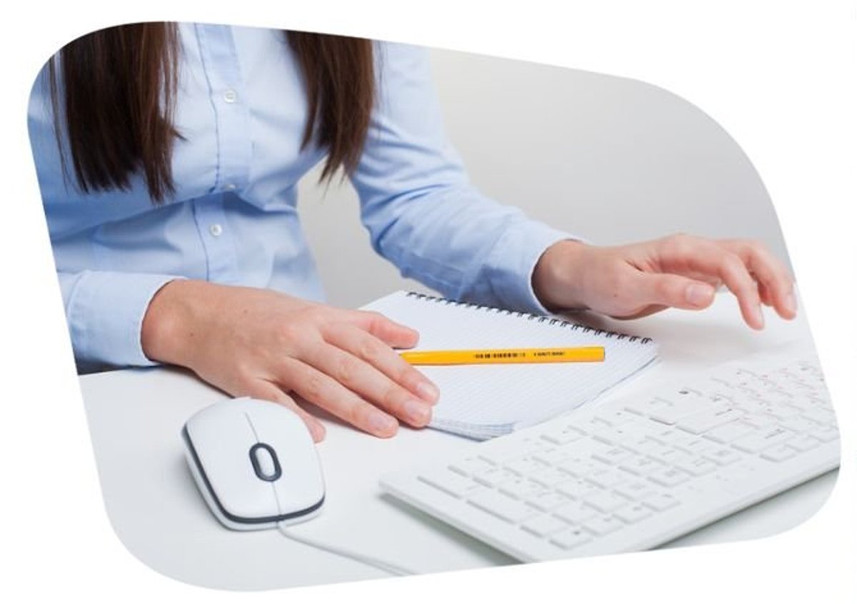 Frau sitzt vor PC Tastatur mit Notizblock und Stift